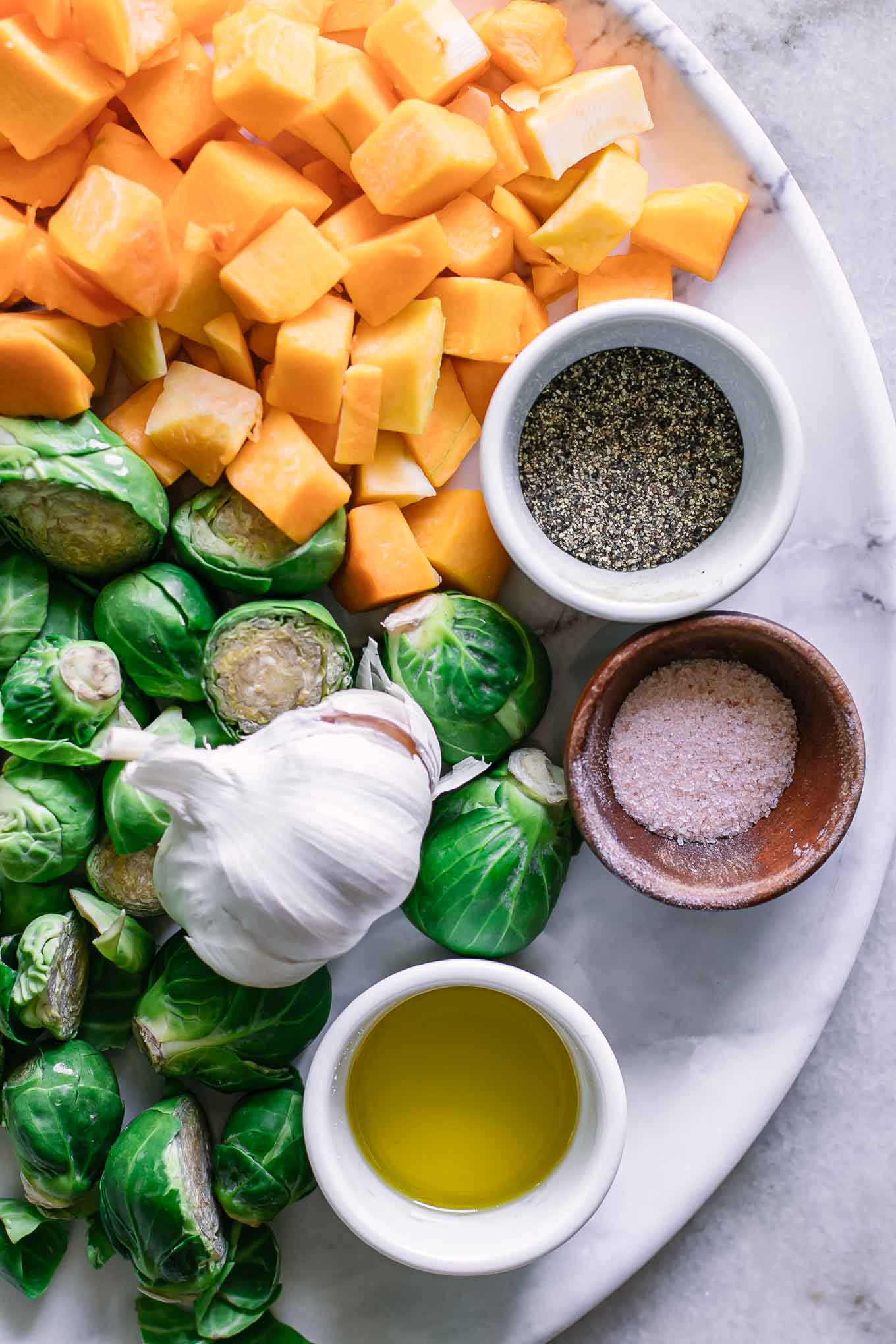 brussels sprouts, butternut squash, garlic, oil, salt, and pepper on a white table
