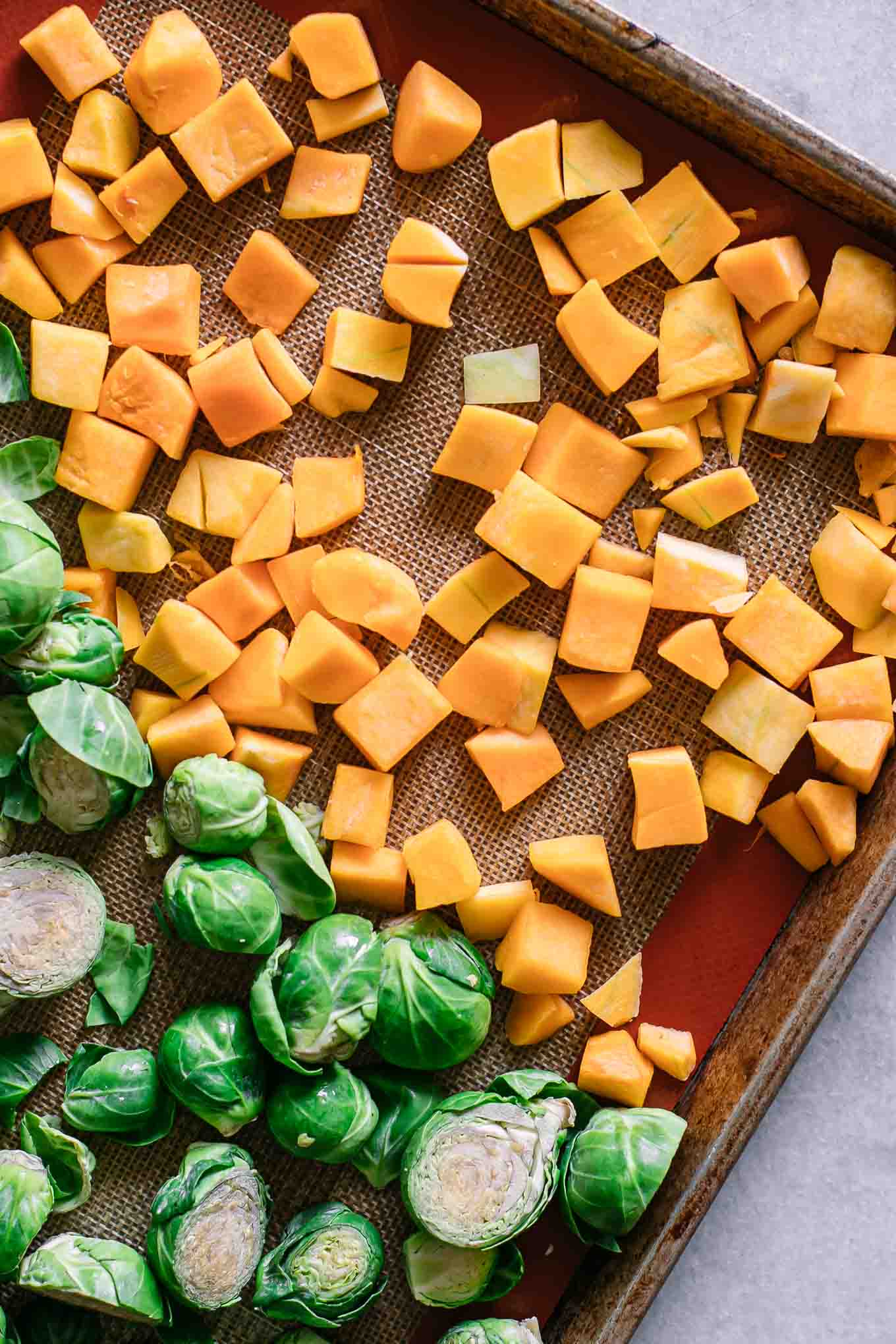 cut butternut squash and brussels sprouts on a baking sheet before roasting