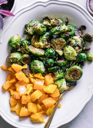 roasted brussels sprouts and butternut squash on a white dish with a gold fork