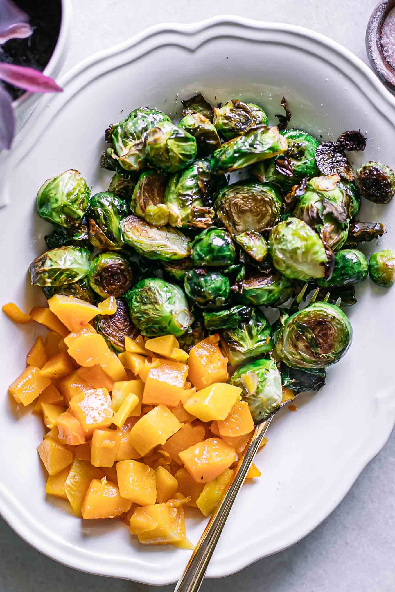 roasted brussels sprouts and butternut squash on a white dish with a gold fork