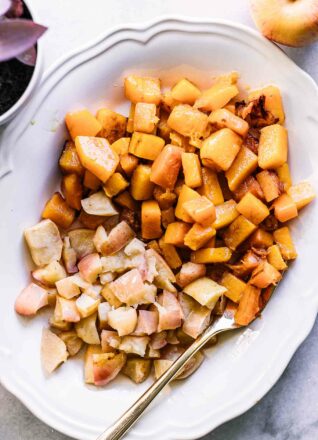 roasted apples and butternut squash on a white plate with a gold fork