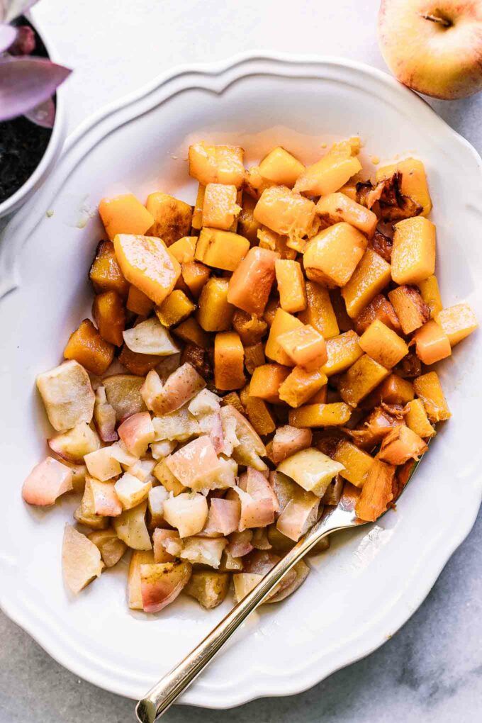 roasted apples and butternut squash on a white plate with a gold fork