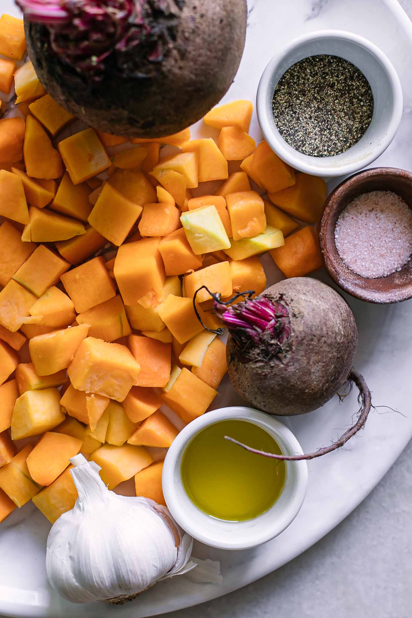 cut butternut squash and beets with garlic on a table with oil, salt, and pepper