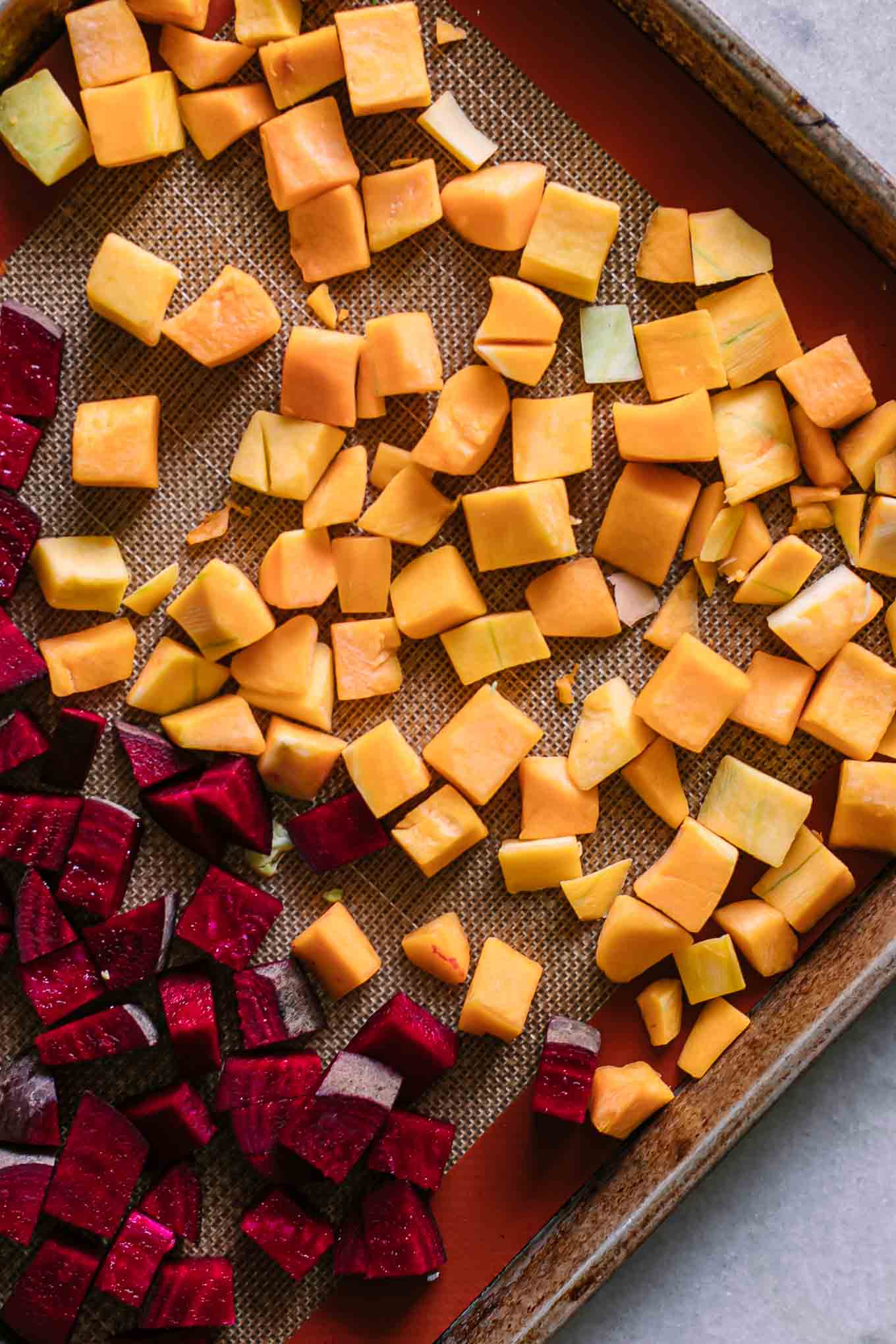 cut butternut squash and beets on a roasting pan before baking