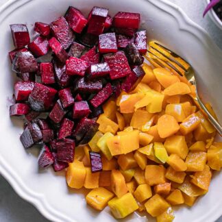 baked butternut squash and beets on a white serving dish with a gold fork