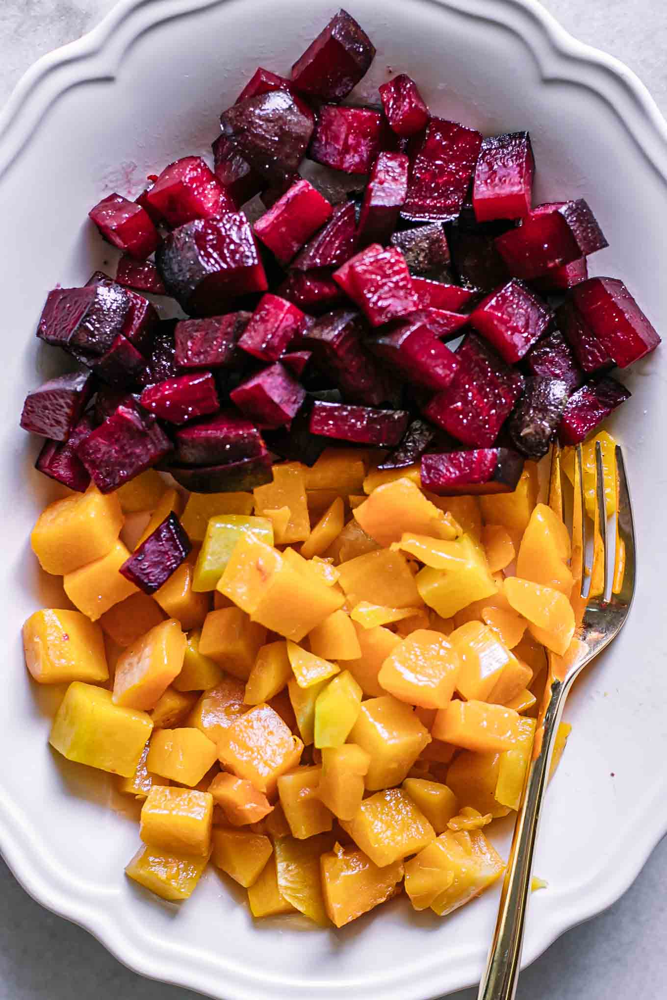 roasted beets and butternut squash on a white plate with a gold fork