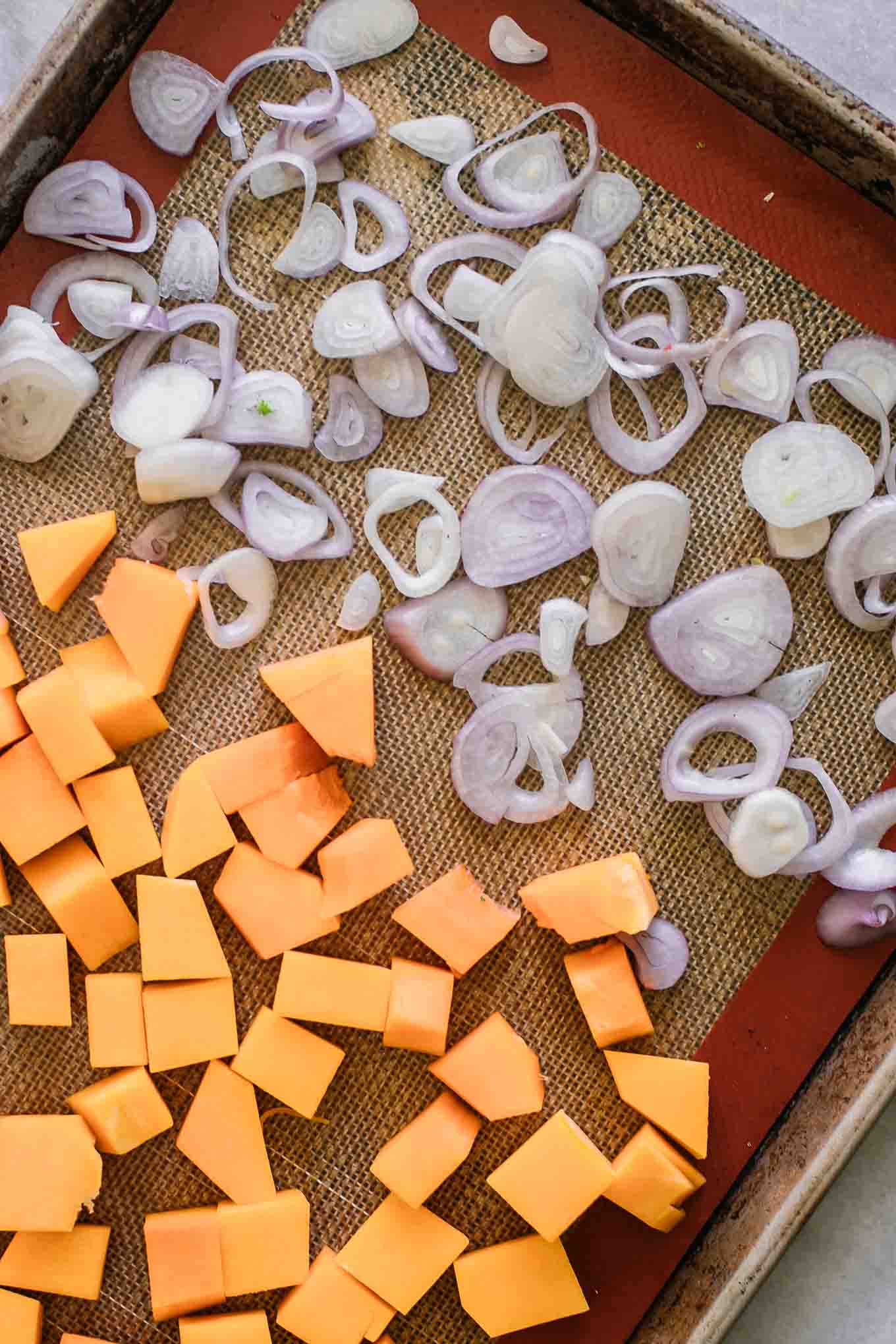 butternut squash cubes and sliced shallots on a baking sheet before roasting