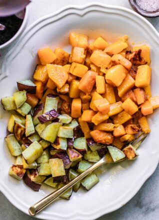 roasted butternut squash and sweet potatoes on a white plate with a gold fork