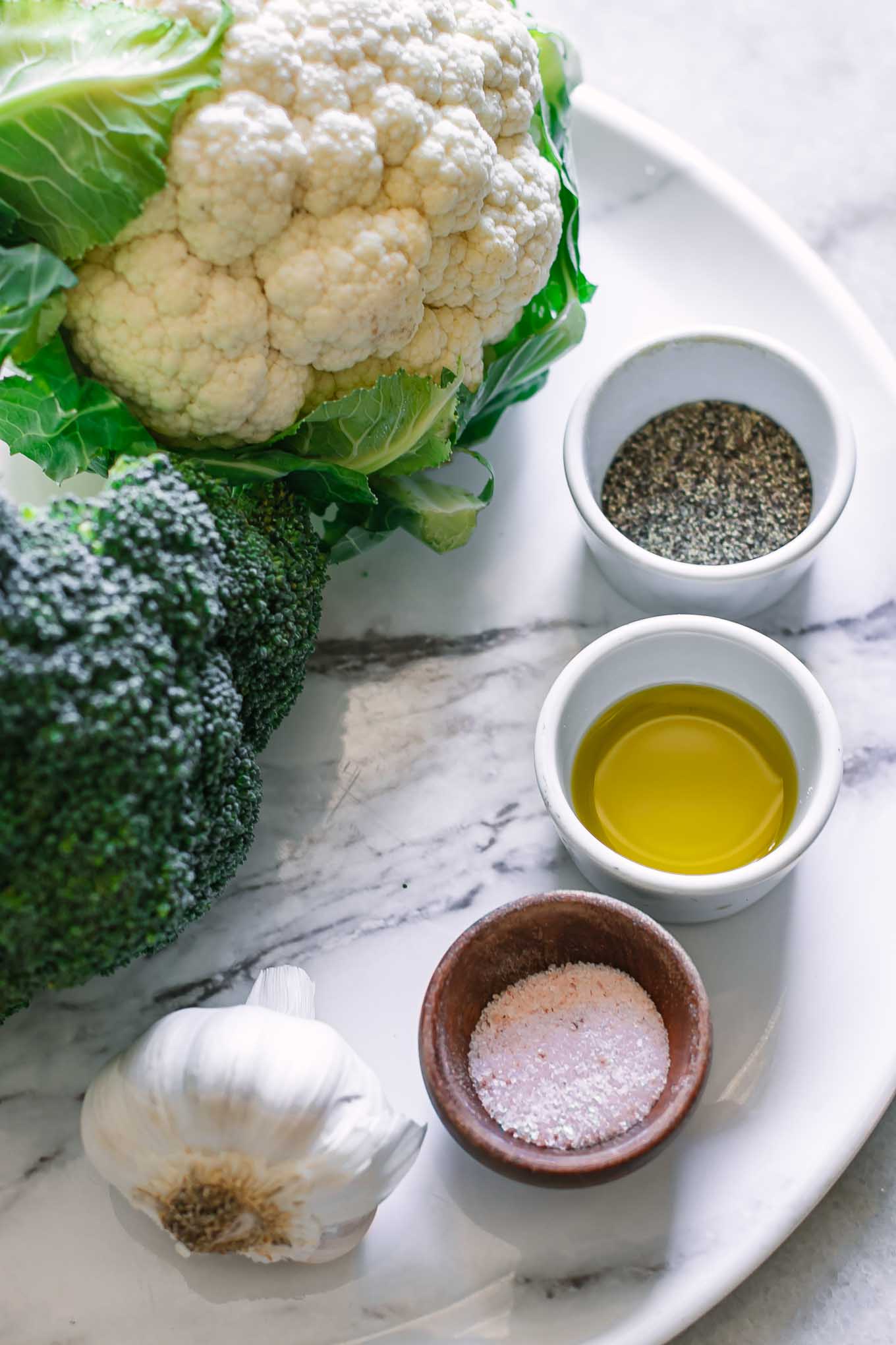 broccoli, cauliflower, garlic, oil, salt, and pepper on a white table