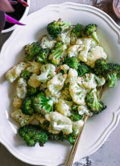 roasted cauliflower and broccoli on a white side dish with a gold fork
