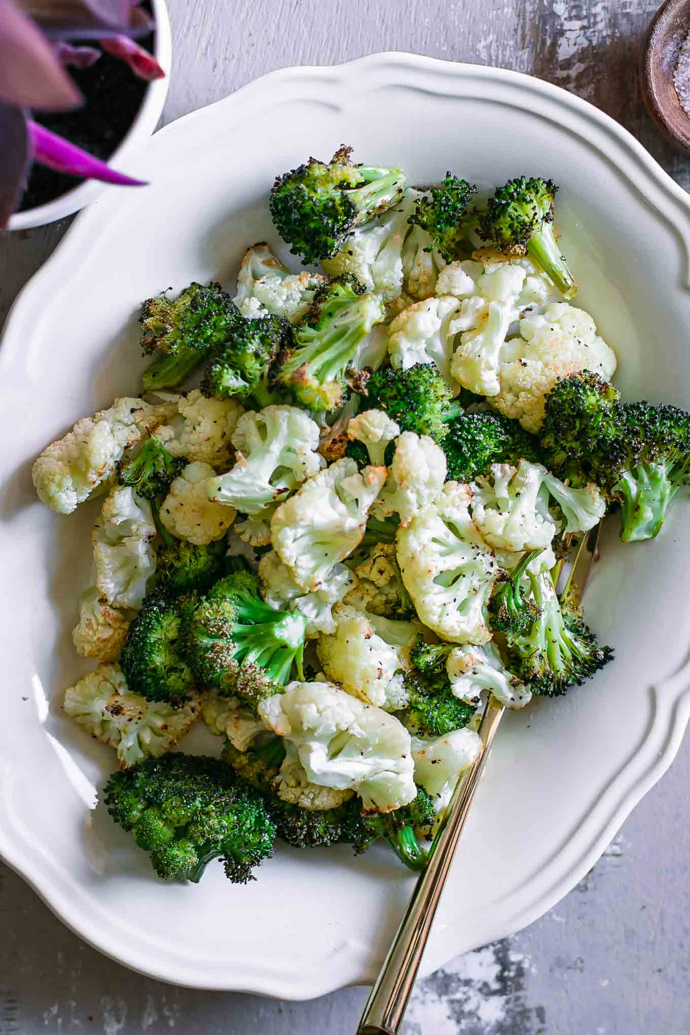 roasted cauliflower and broccoli on a white side dish with a gold fork