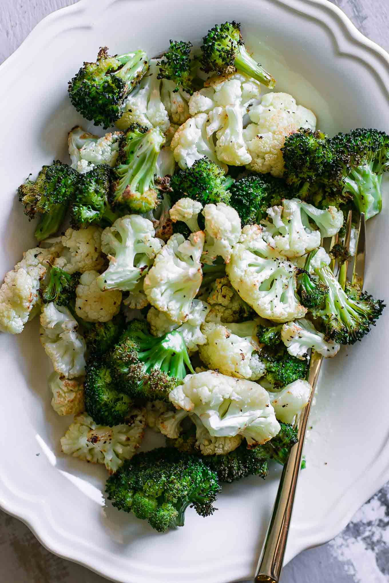 a close up photo of baked broccoli and cauliflower on a white plate