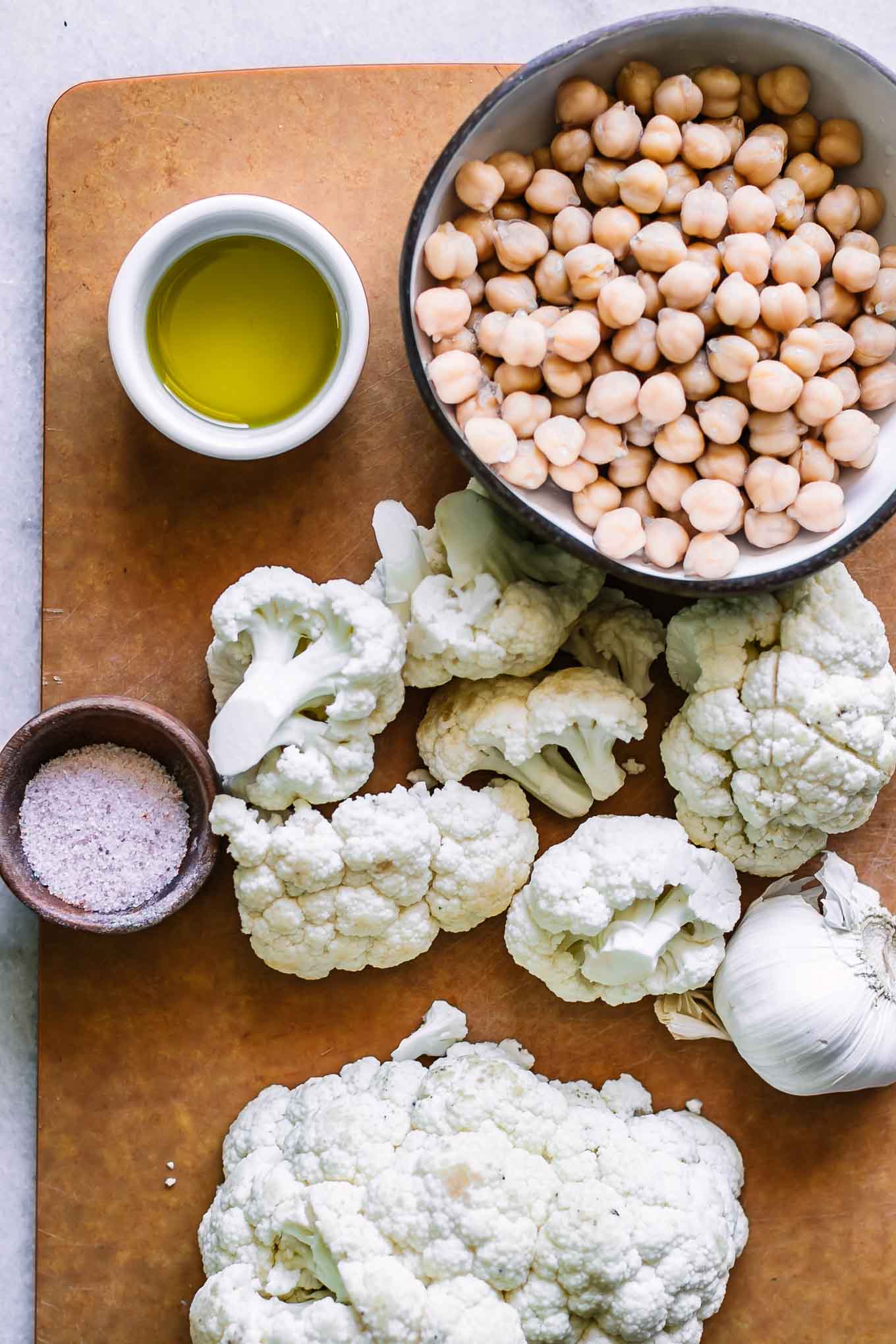 cut cauliflower on a cutting board with a bowl of chickpeas