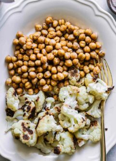 a close up photo of baked cauliflower and chickpeas on a white plate with a gold fork