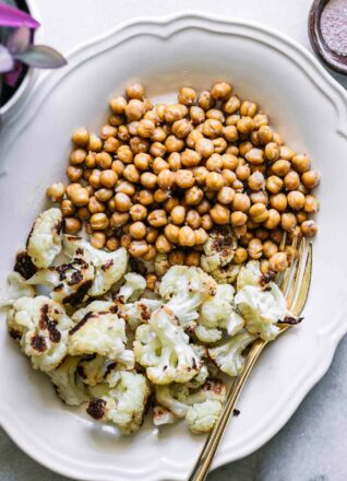 roasted cauliflower and chickpeas on a white plate with a gold fork