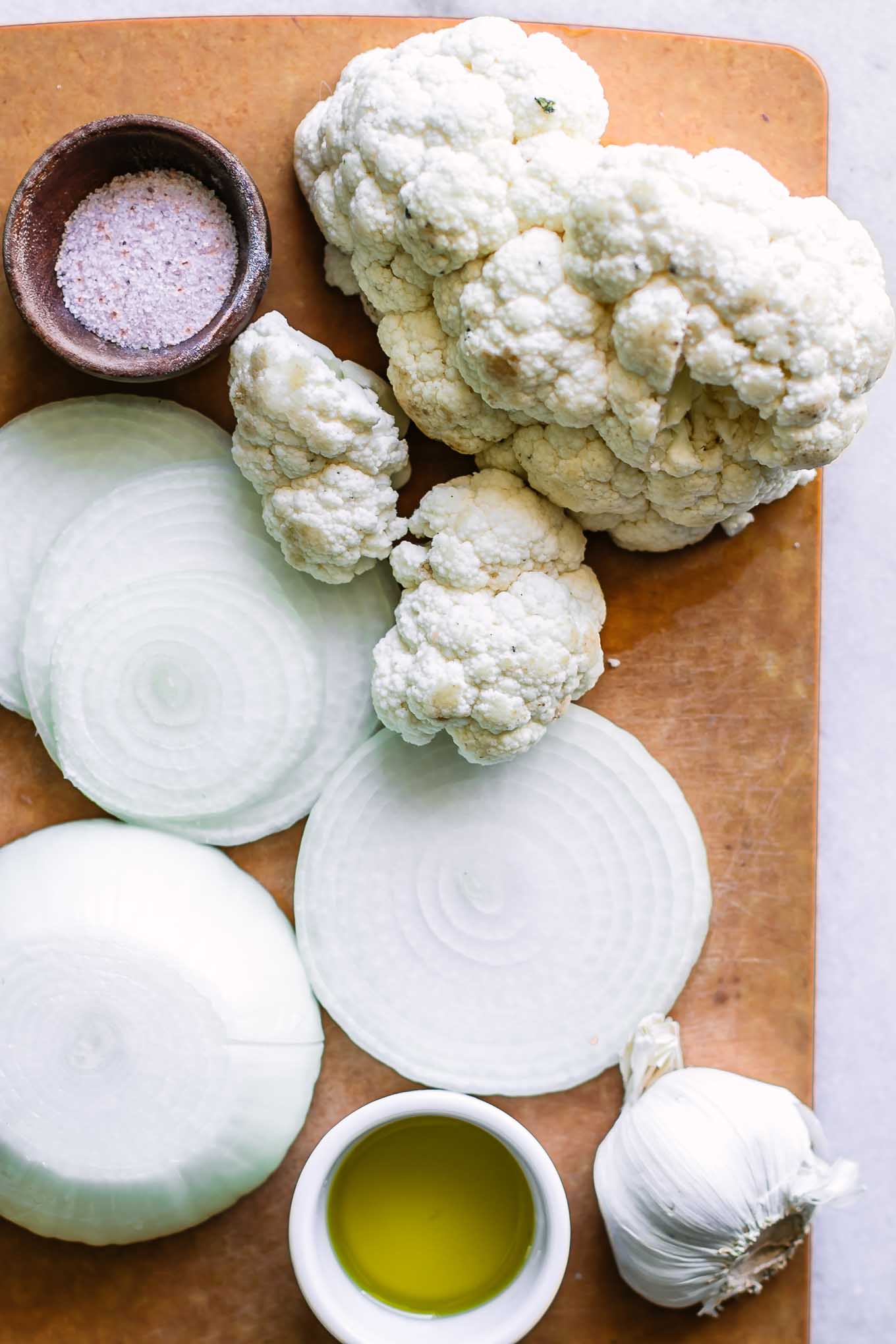 cut cauliflower florets on a cutting board with an onion