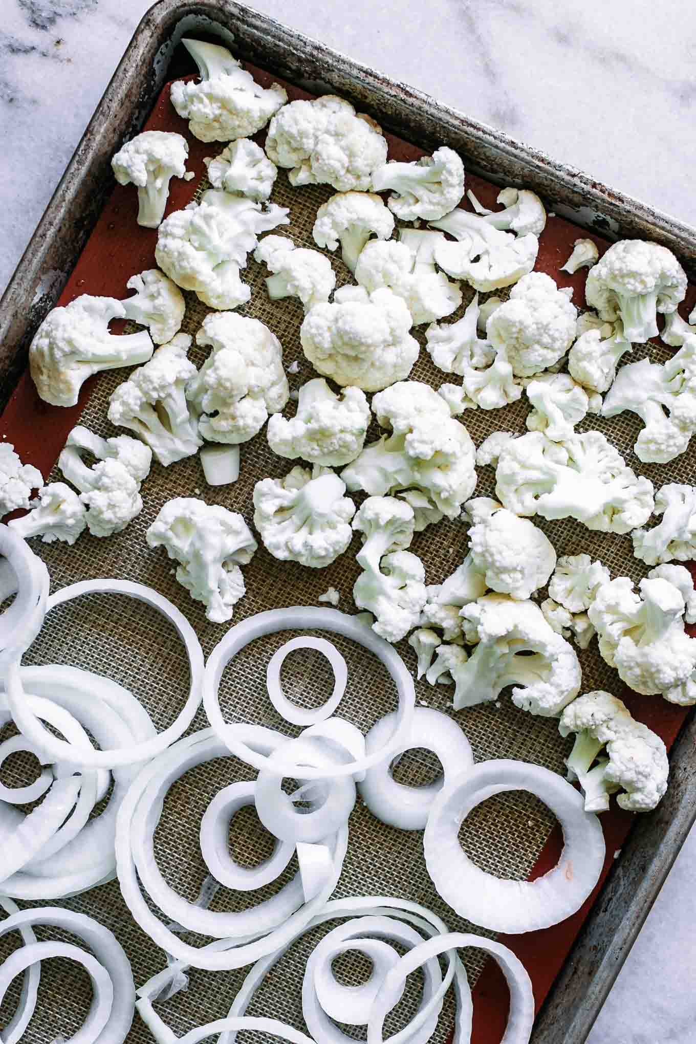 cauliflower florets and onions slices on a baking sheet before roasting