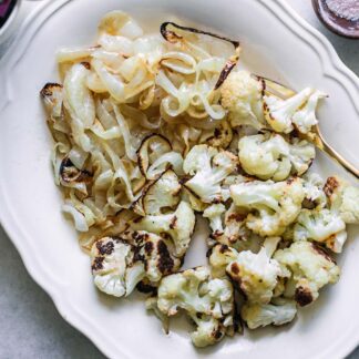 a white side dish of roasted onions and cauliflower on a table