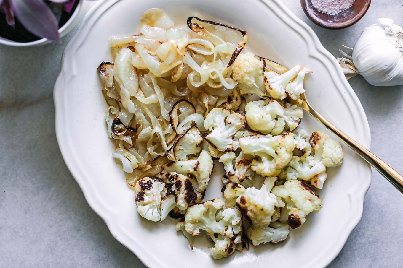 a white side dish of roasted onions and cauliflower on a table