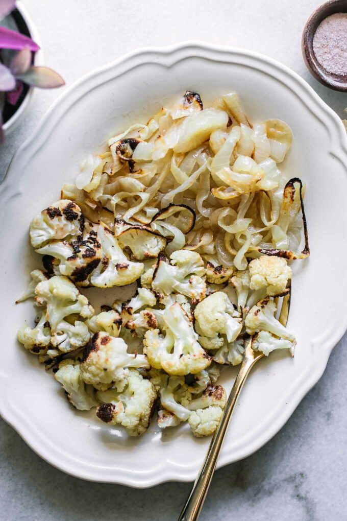 roasted cauliflower and onions on a white plate with a gold fork