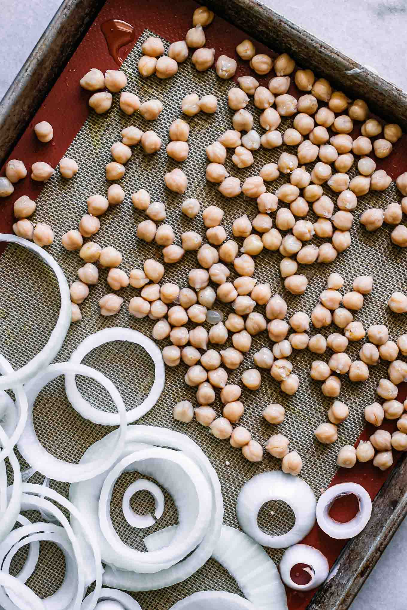 chickpeas and sliced onions on a baking sheet before roasting