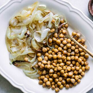 a white plate with baked chickpeas and onions on a white table