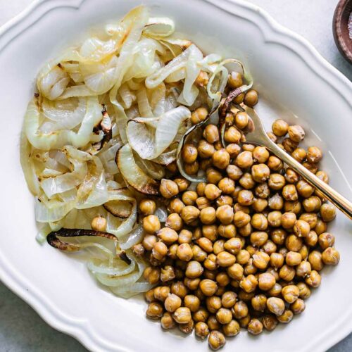 a white plate with baked chickpeas and onions on a white table