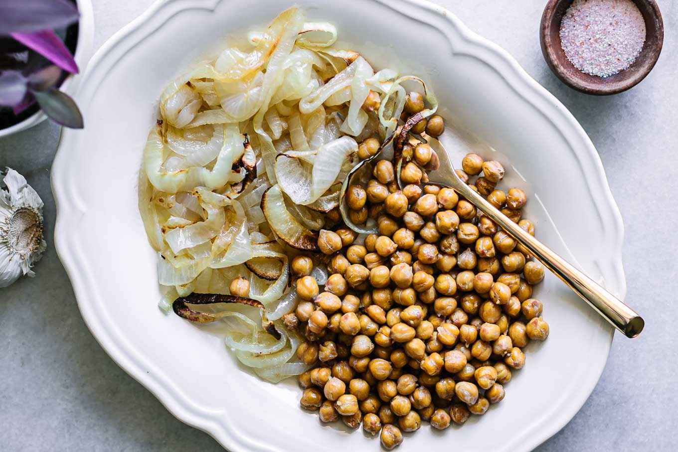 a white plate with baked chickpeas and onions on a white table
