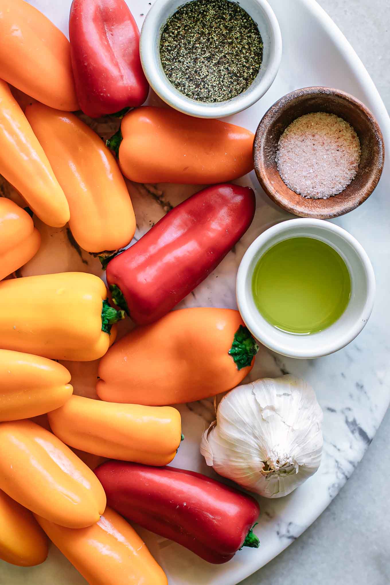 colorful mini sweet peppers on a table with bowls of oil, salt, pepper, and garlic