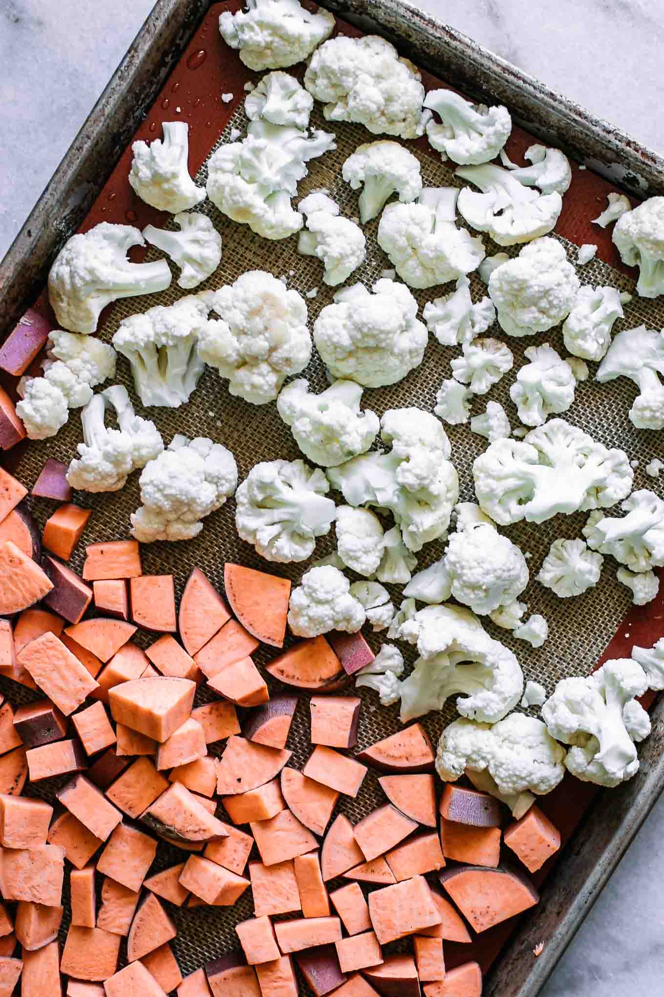 cut sweet potatoes and cauliflower florets on a baking sheet before roasting