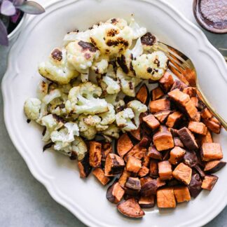 baked cauliflower and sweet potatoes on a white serving dish with a gold fork