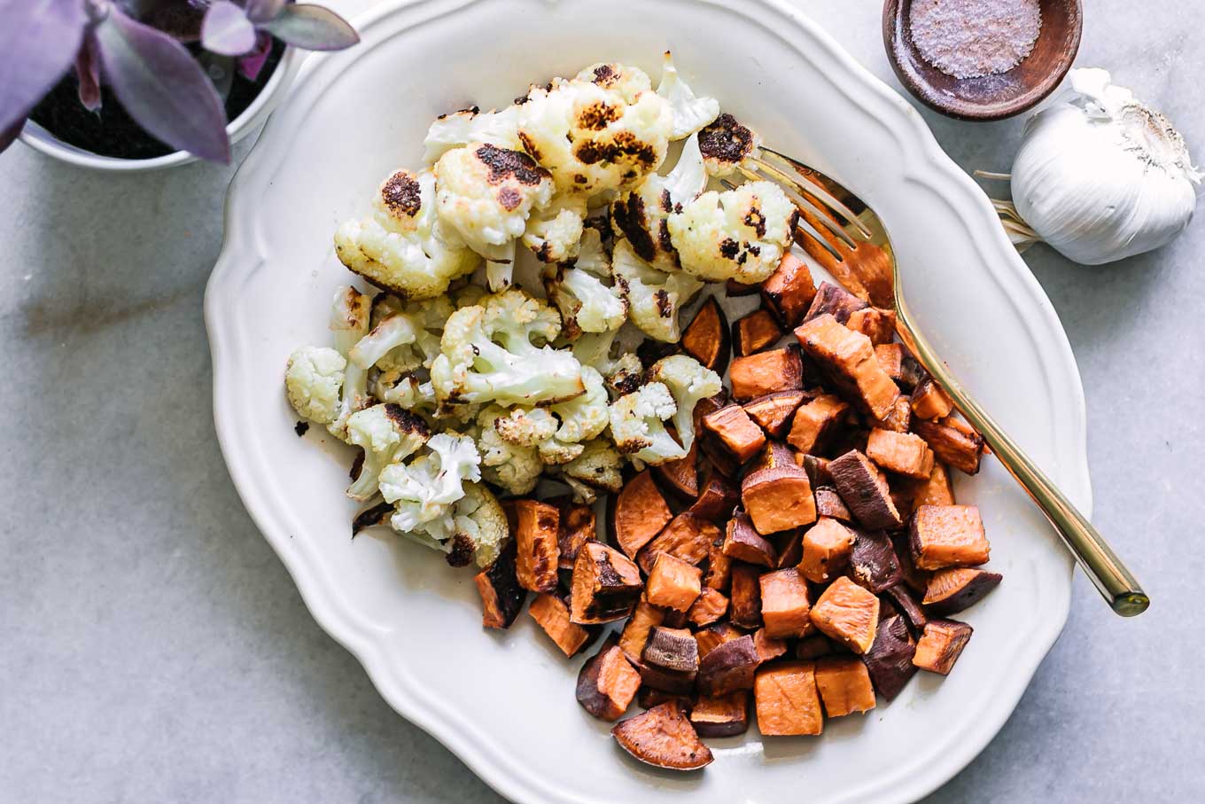 baked cauliflower and sweet potatoes on a white serving dish with a gold fork