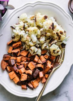 roasted sweet potatoes and cauliflower on a white plate with a white fork
