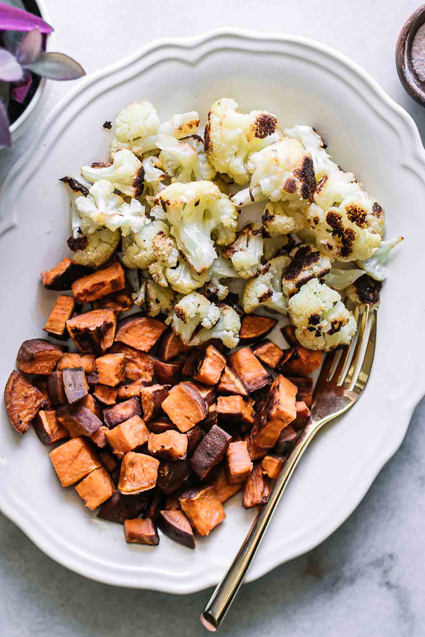 roasted sweet potatoes and cauliflower on a white plate with a white fork