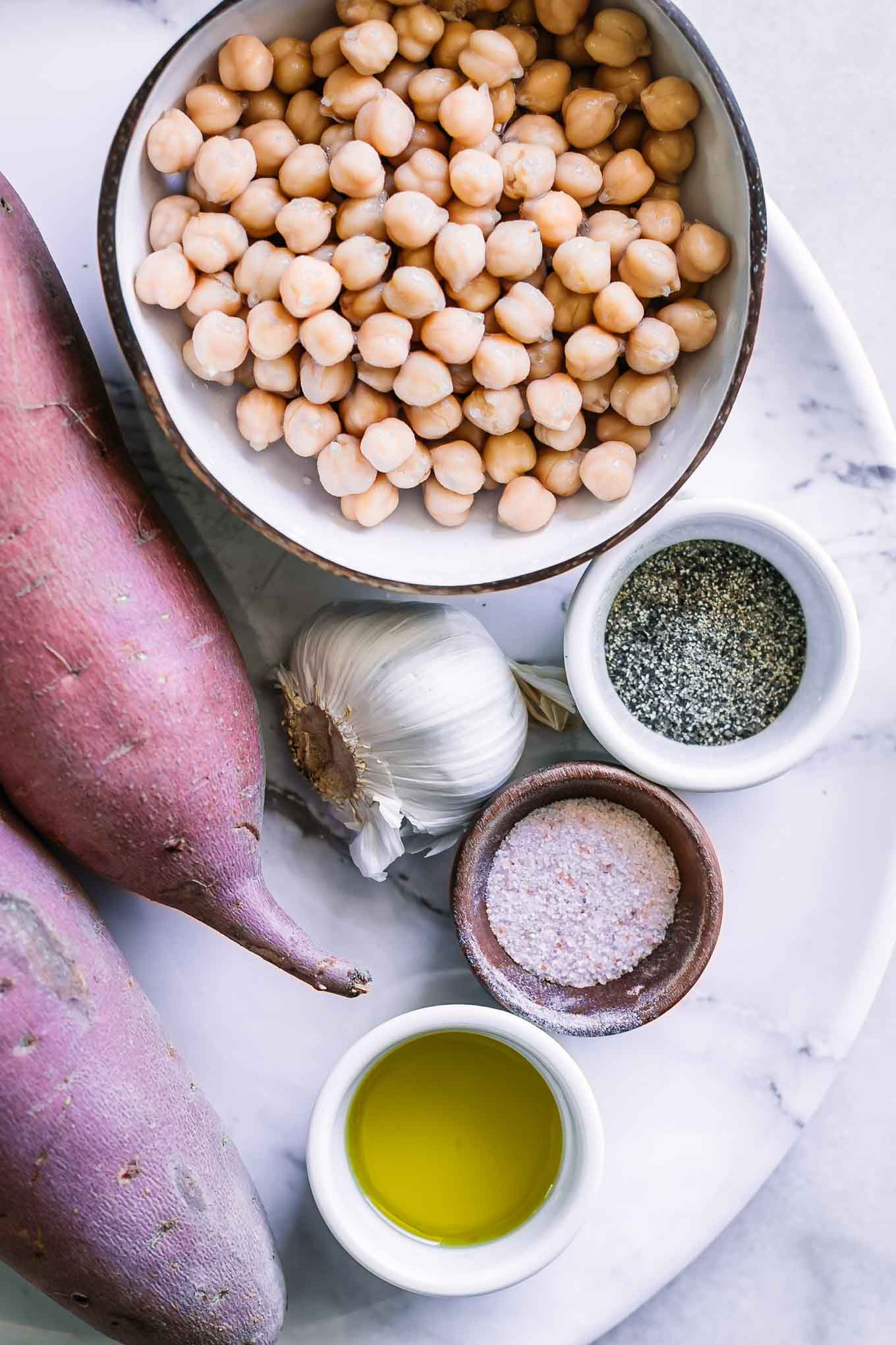 sweet potatoes and a bowl of chickpeas, garlic, oil, salt, and pepper on a white table