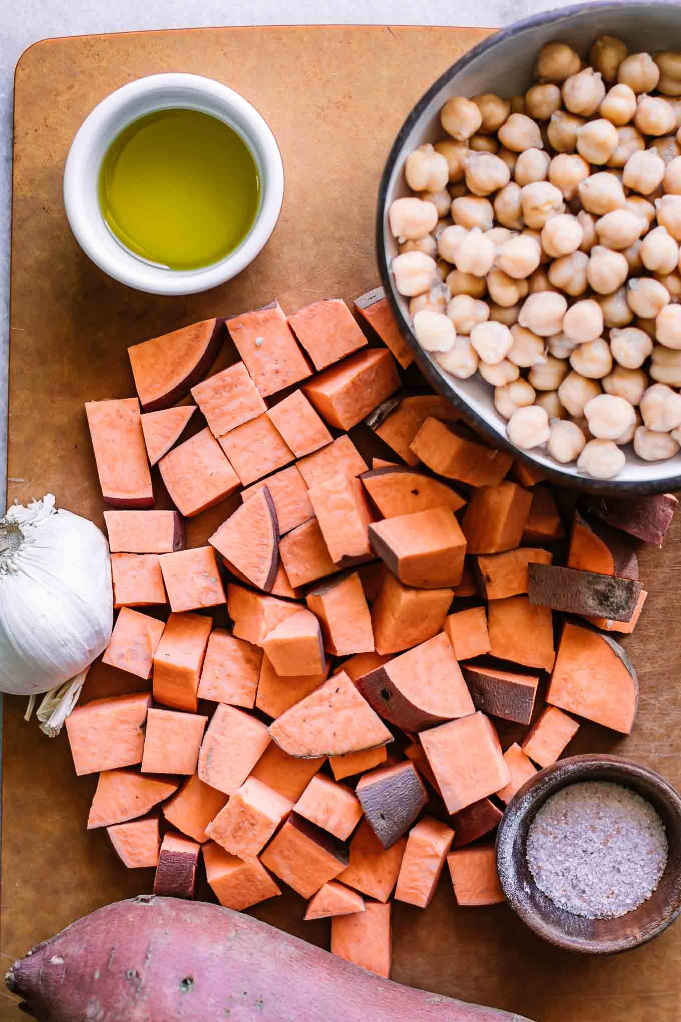 cut sweet potatoes on a cutting board with a bowl of chickpeas