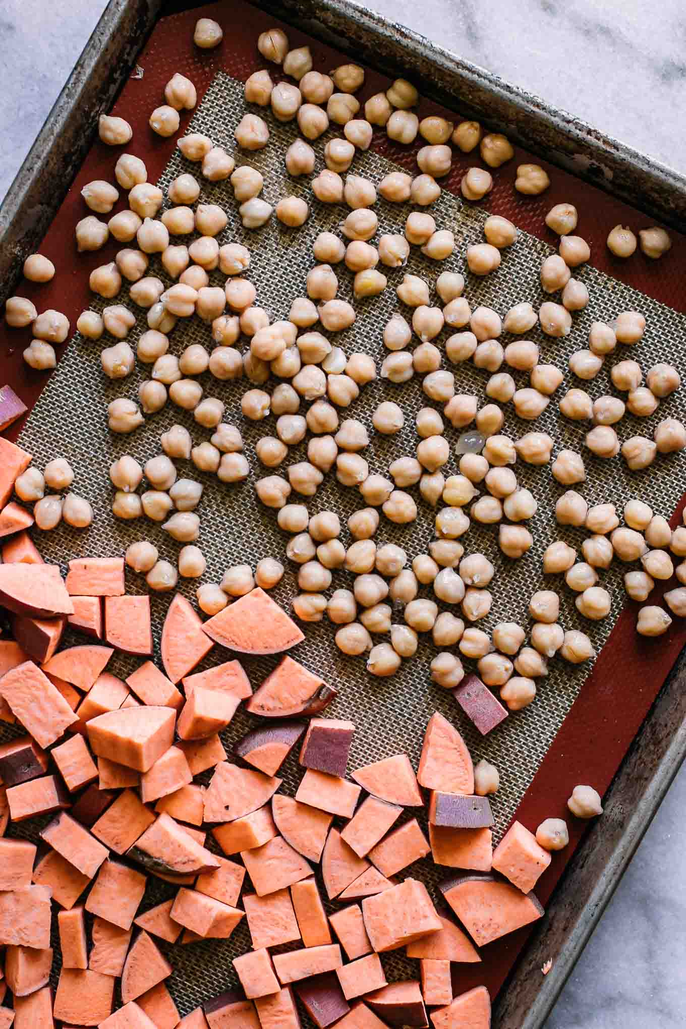 a roasting pan with cut sweet potatoes and chickpeas before baking