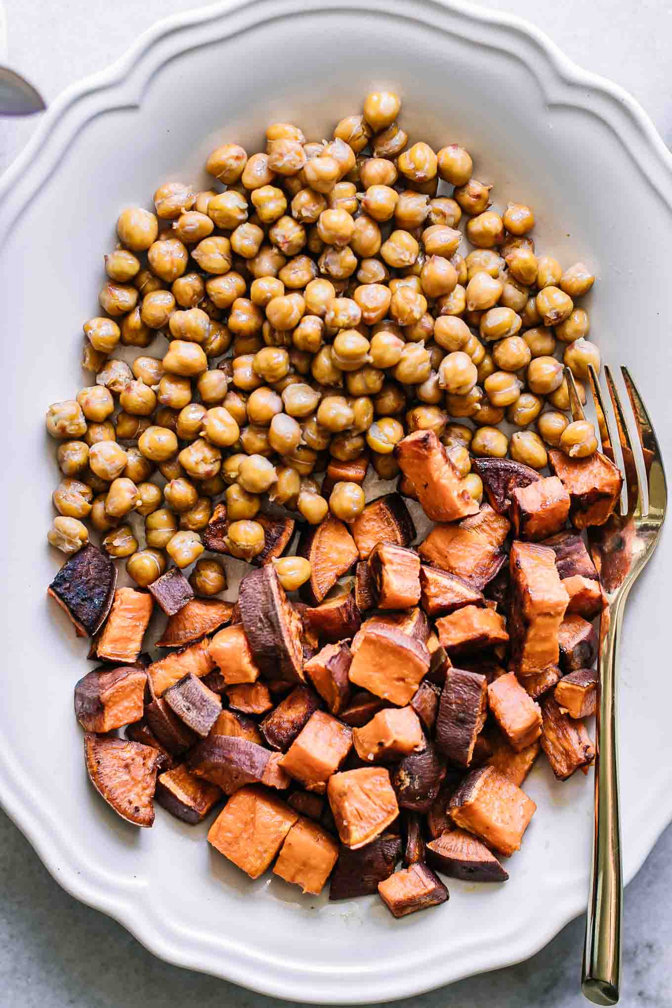 a white plate with baked chickpeas and sweet potatoes and a gold fork
