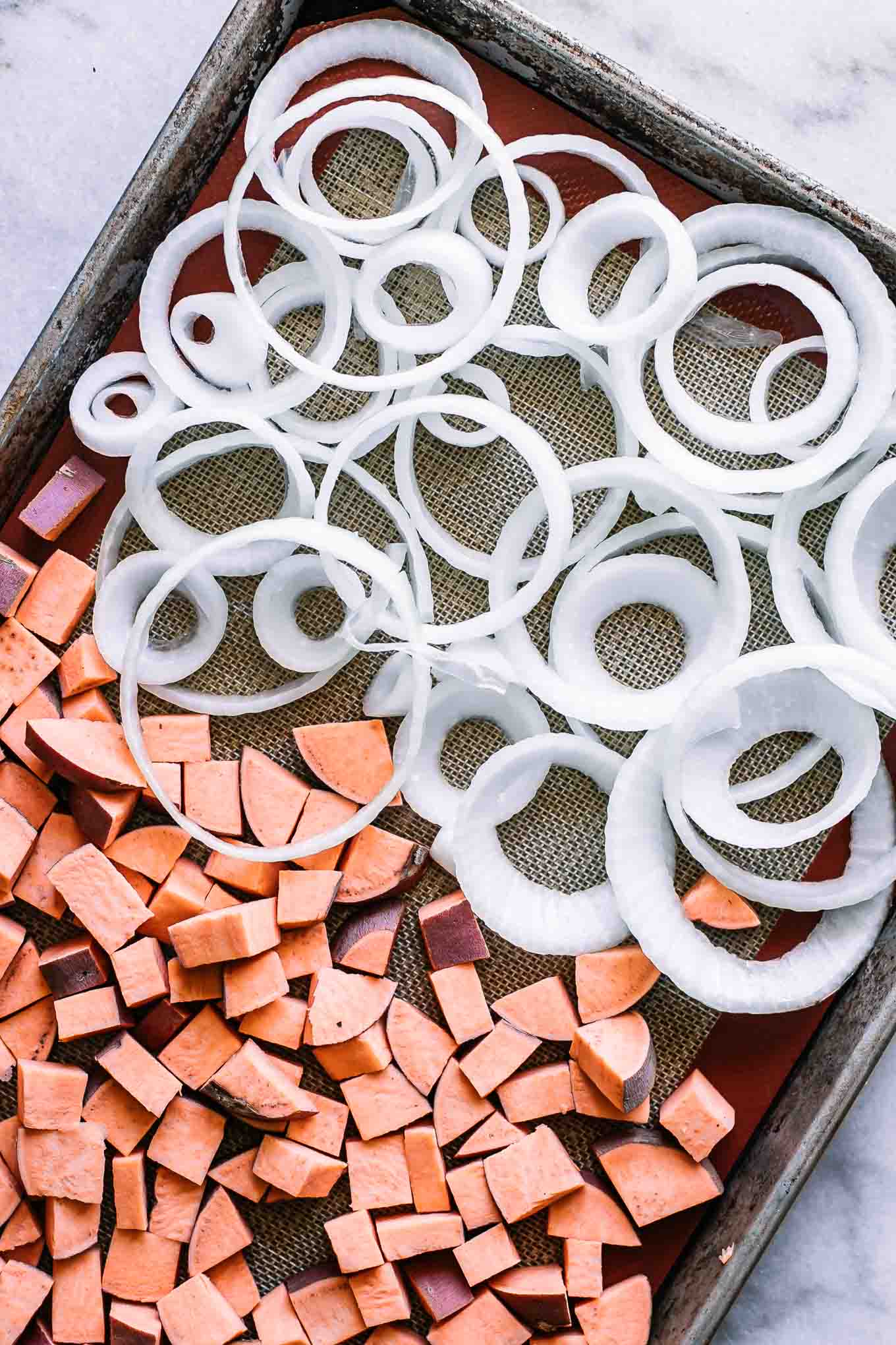 cut sweet potatoes and sliced onions on a sheet pan before baking