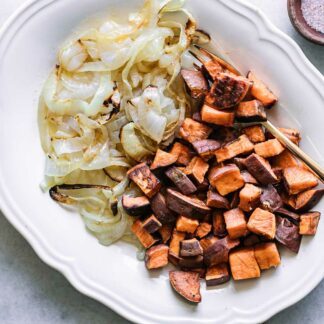 baked sweet potatoes and onions on a white side dish and gold fork