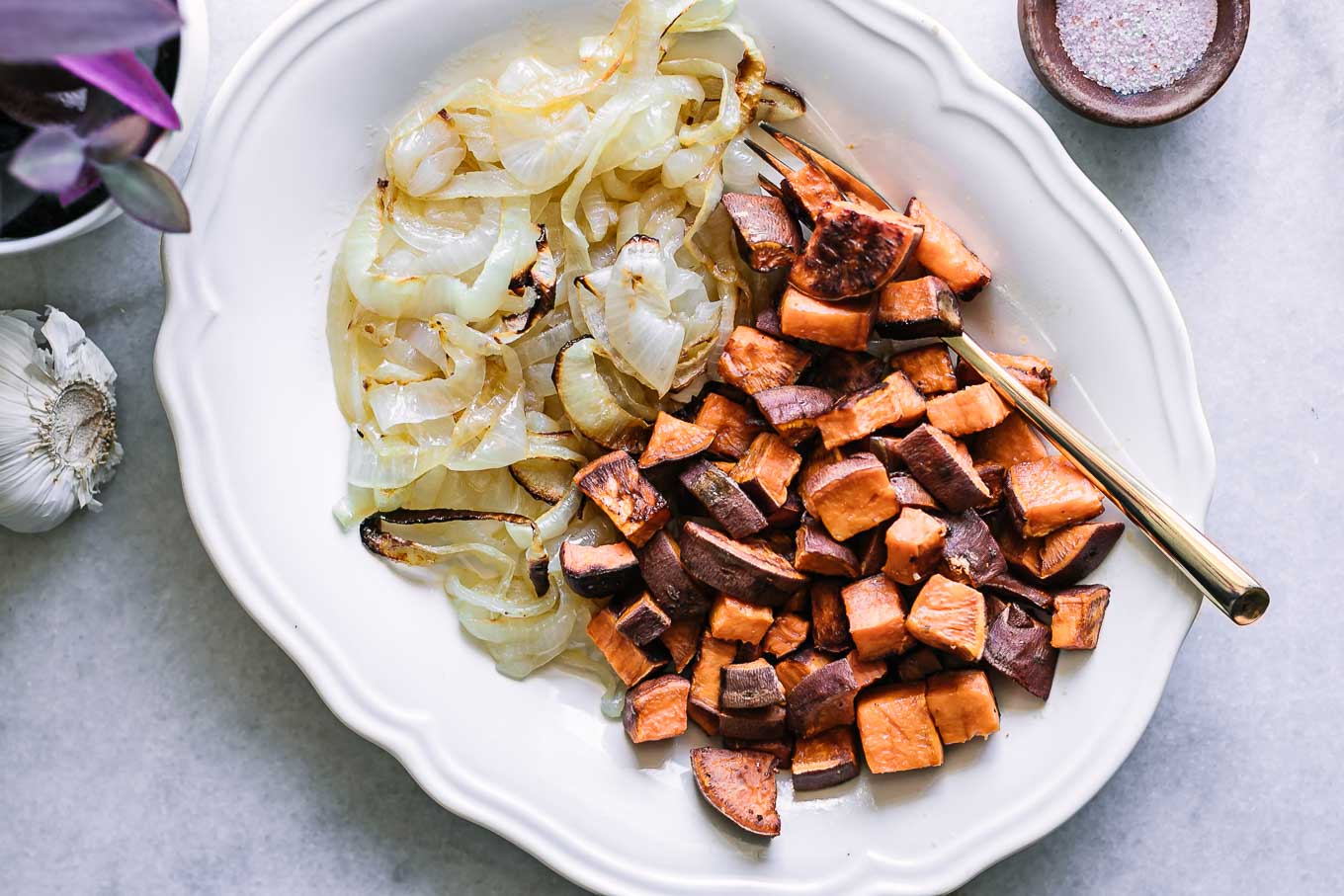 baked sweet potatoes and onions on a white side dish and gold fork