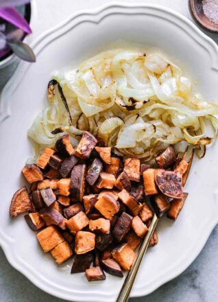 roasted sweet potatoes and roasted onions on a white serving dish with a gold fork