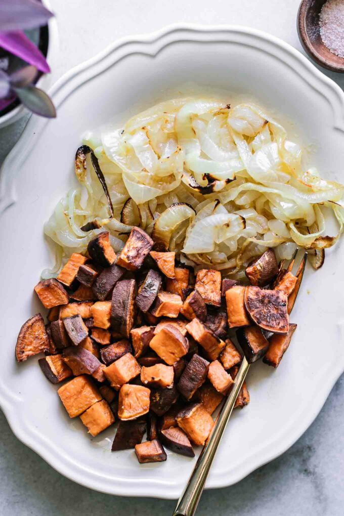 roasted sweet potatoes and roasted onions on a white serving dish with a gold fork