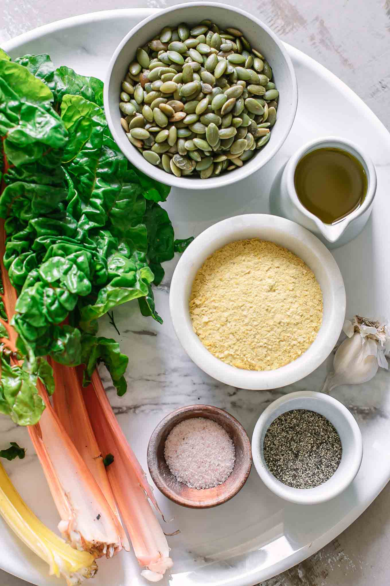 chard leaves, nuts, garlic, cheese, oil, salt, and pepper for pesto on a white table