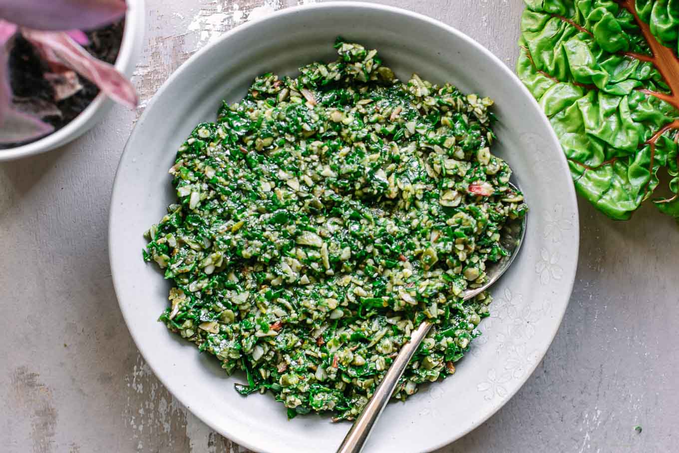 a bowl with chard pesto sauce on a wood table and fresh chard leaves