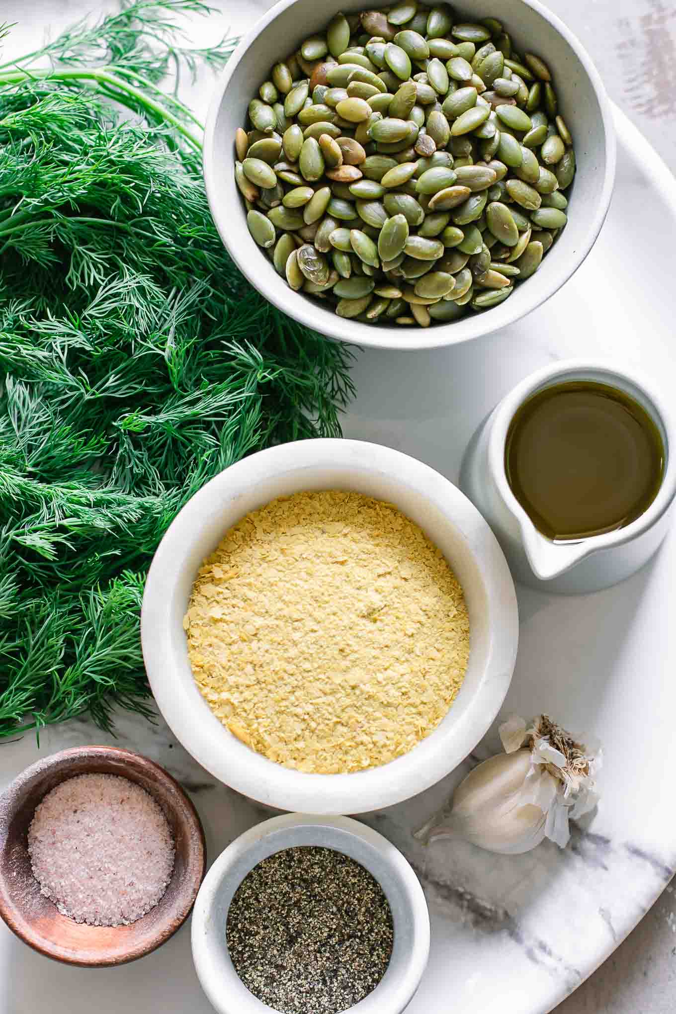 fresh dill, nuts, garlic, cheese, oil, salt, and pepper on a white table for pesto