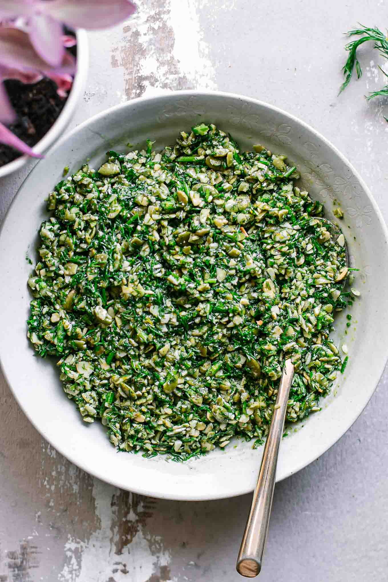 dill pesto sauce in a white bowl with a gold fork on a white table