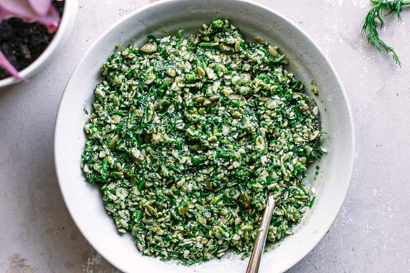 pesto with fresh dill inside white side dish bowl with a gold fork