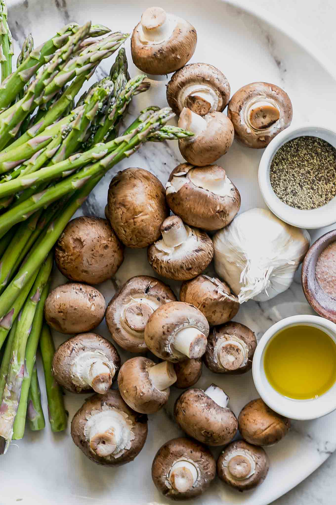 mushrooms, asparagus, garlic, oil, salt, and pepper on a white table