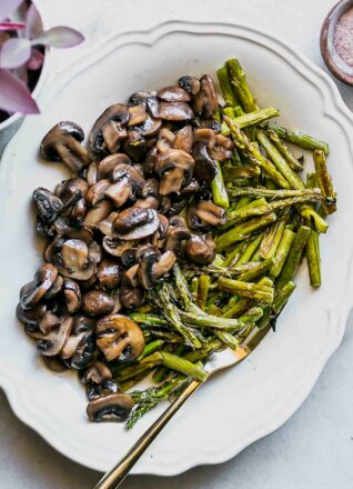 roasted mushrooms and asparagus on a white plate with a gold fork